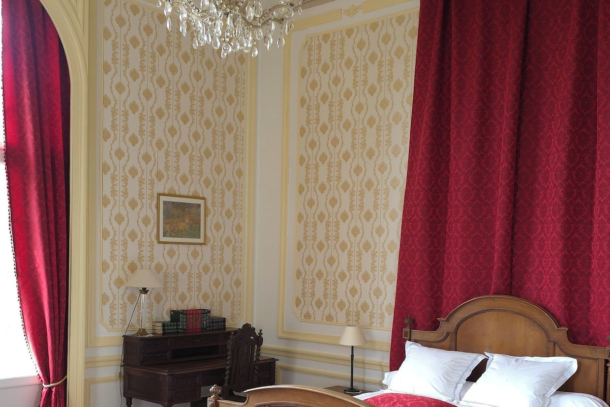 Un dormitorio tradicional con una cama de madera, un banco, una araña y papel tapiz estampado.