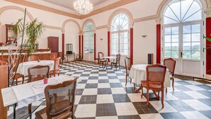 A spacious dining area with checkered flooring, multiple tables, and chairs, large arched windows, and a chandelier. - Chateau de Pourpry (Damiatte)