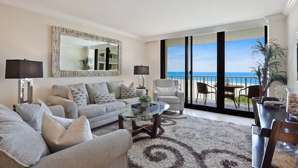 A living room with a sofa, armchairs, a coffee table, and a view of the ocean through large sliding doors. - Condo on Beach | Pool, Gym & Tennis Courts (Marco Island)