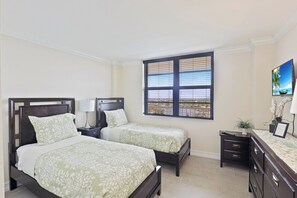 A bedroom with two beds, a nightstand, a dresser, a window with blinds, and a painting on the wall.