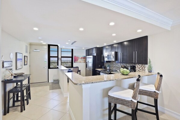 A modern kitchen with dark cabinets, a granite countertop, and a central island with bar stools.