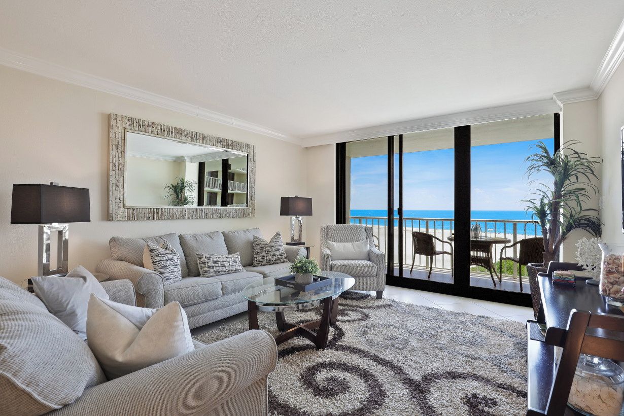 A living room with a sofa, armchairs, a coffee table, and a view of the ocean through large sliding doors.