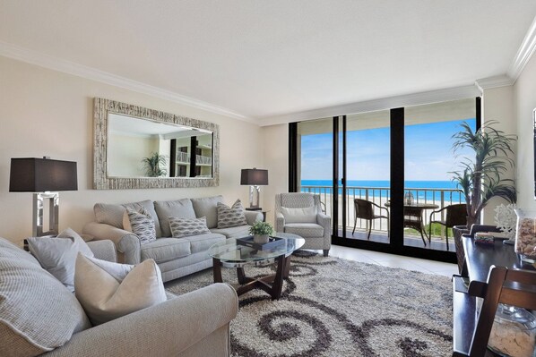 A living room with a sofa, armchairs, a coffee table, and a view of the ocean through large sliding doors.