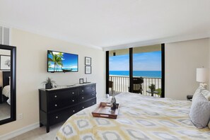 A bedroom with a bed, a dresser, a TV, and a balcony with a view of the ocean.
