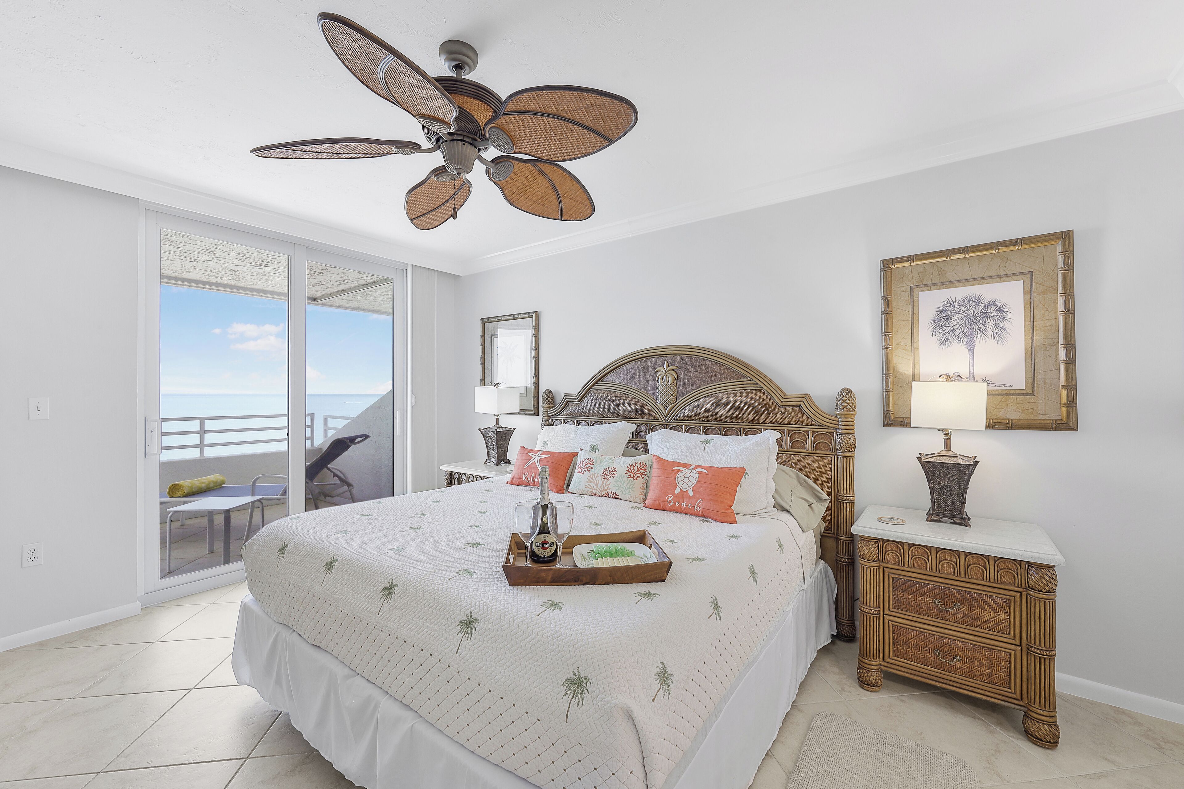 A bedroom with a bed, a nightstand, a ceiling fan, a window with a view, and a door to a balcony.