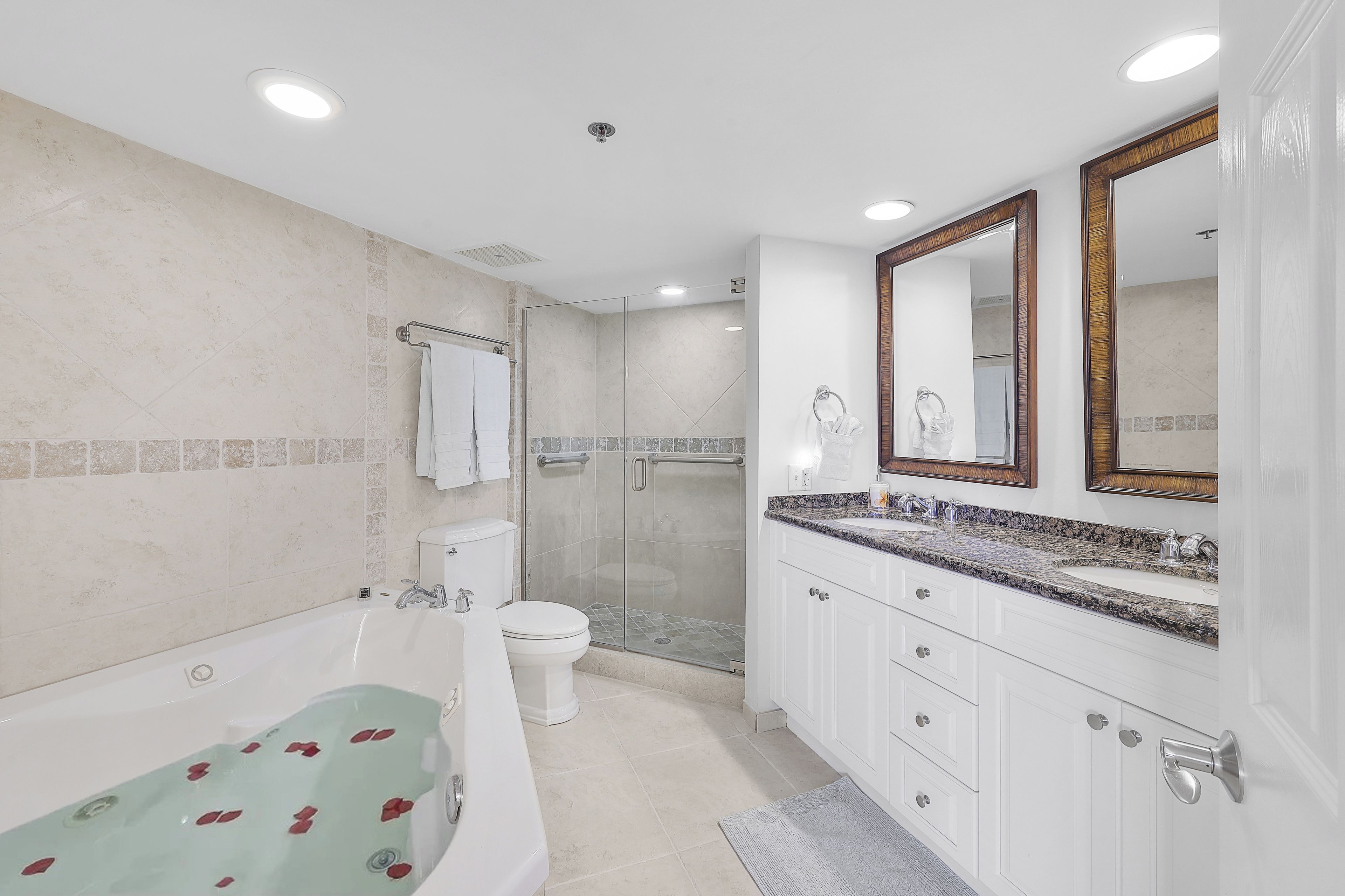 A modern bathroom with a bathtub, toilet, shower, and double vanity with a large mirror.
