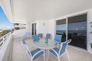 A balcony with a glass table and chairs, a bottle of water, and a view of the city. - Beachfront Condo | Views, Pools & Tennis Courts (Marco Island)