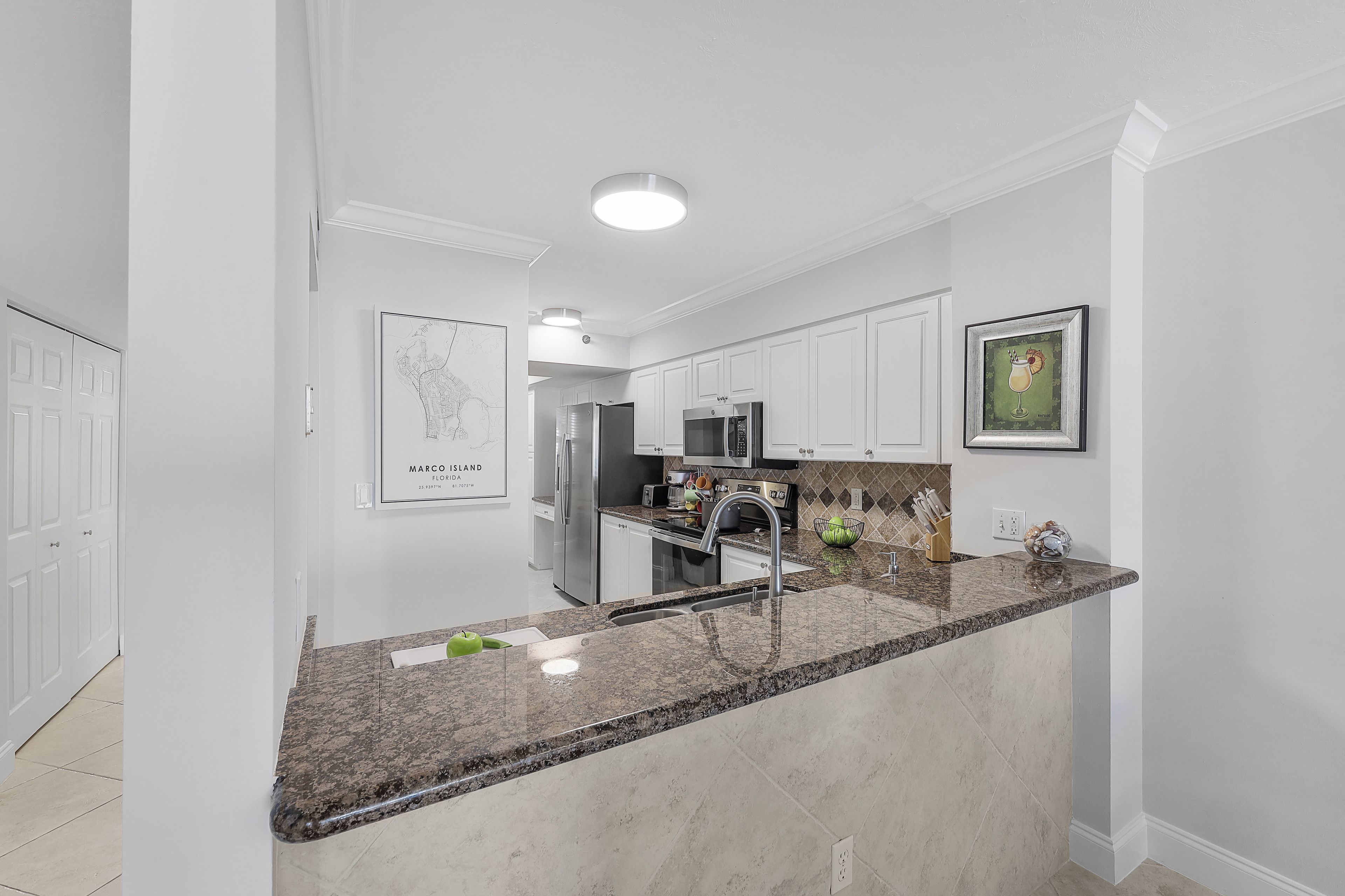 Een moderne keuken met witte kasten, granieten aanrechtbladen, roestvrijstalen apparatuur en een centraal keukenblok met een spoelbak.