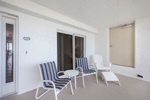 A balcony with three chairs, one striped and two plain, and a small table.