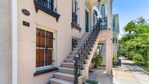 Un edificio con una escalera que lleva al segundo piso, una planta grande en maceta y un cielo despejado.