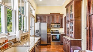 Una cocina con armarios de madera, electrodomésticos de acero inoxidable, encimera de granito y una ventana con vistas a árboles.