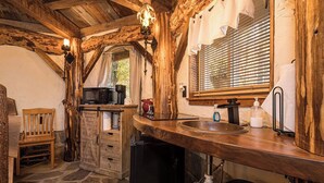 Eine rustikale Küche mit Holzbalken, Steinboden, einer Holzbank, einer Mikrowelle, einem Spülbecken und einem Fenster mit Jalousien.