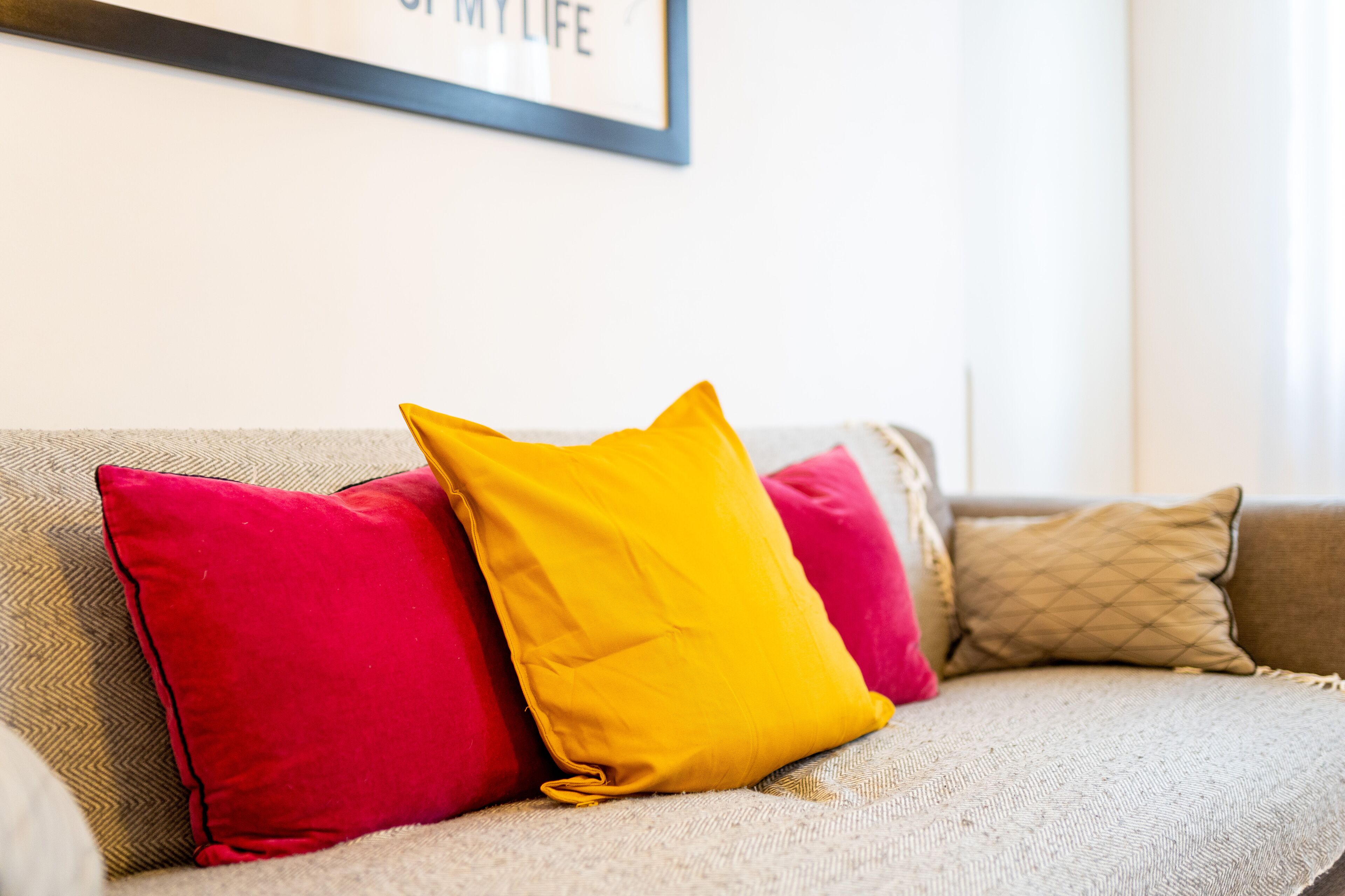 A beige sofa with three pillows: two red and one yellow.