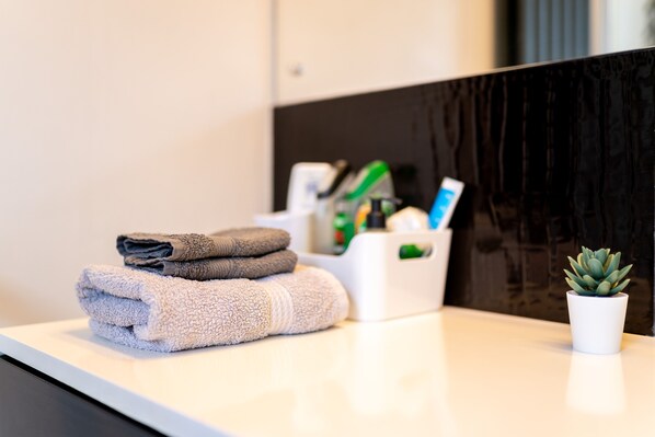 A neatly arranged bathroom with towels, a potted plant, and toiletries on a counter. - Le Cwtch - Beautiful 1 Bed Apartment (Cardiff)