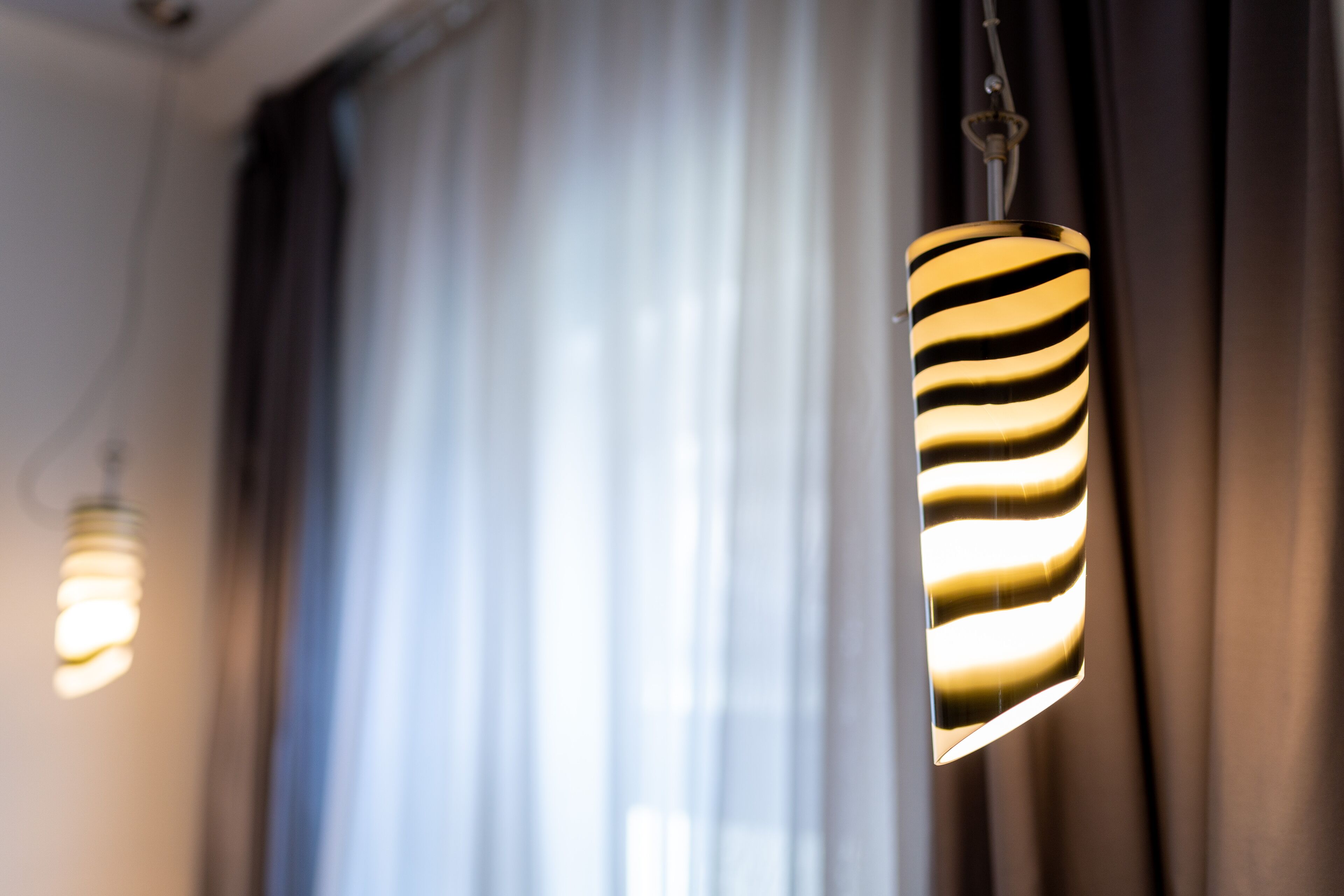 A room with a window, curtains, and a hanging lamp.
