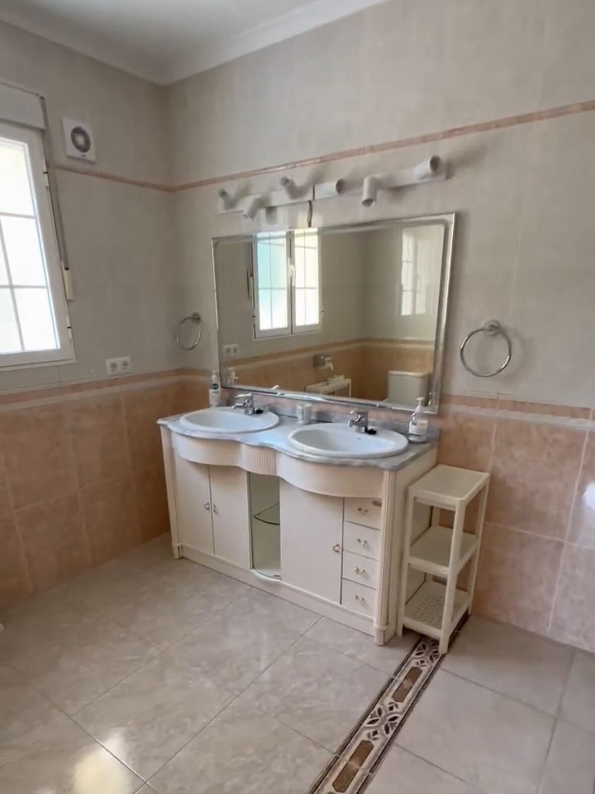 A bathroom with two sinks, a large mirror, a small stool, and a window.