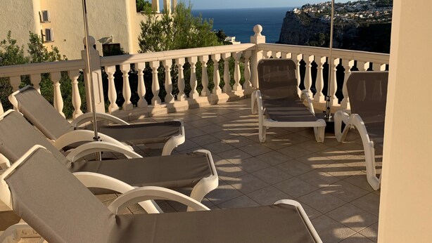 Een balkon met witte stoelen en twee parasols, met uitzicht op de kust.