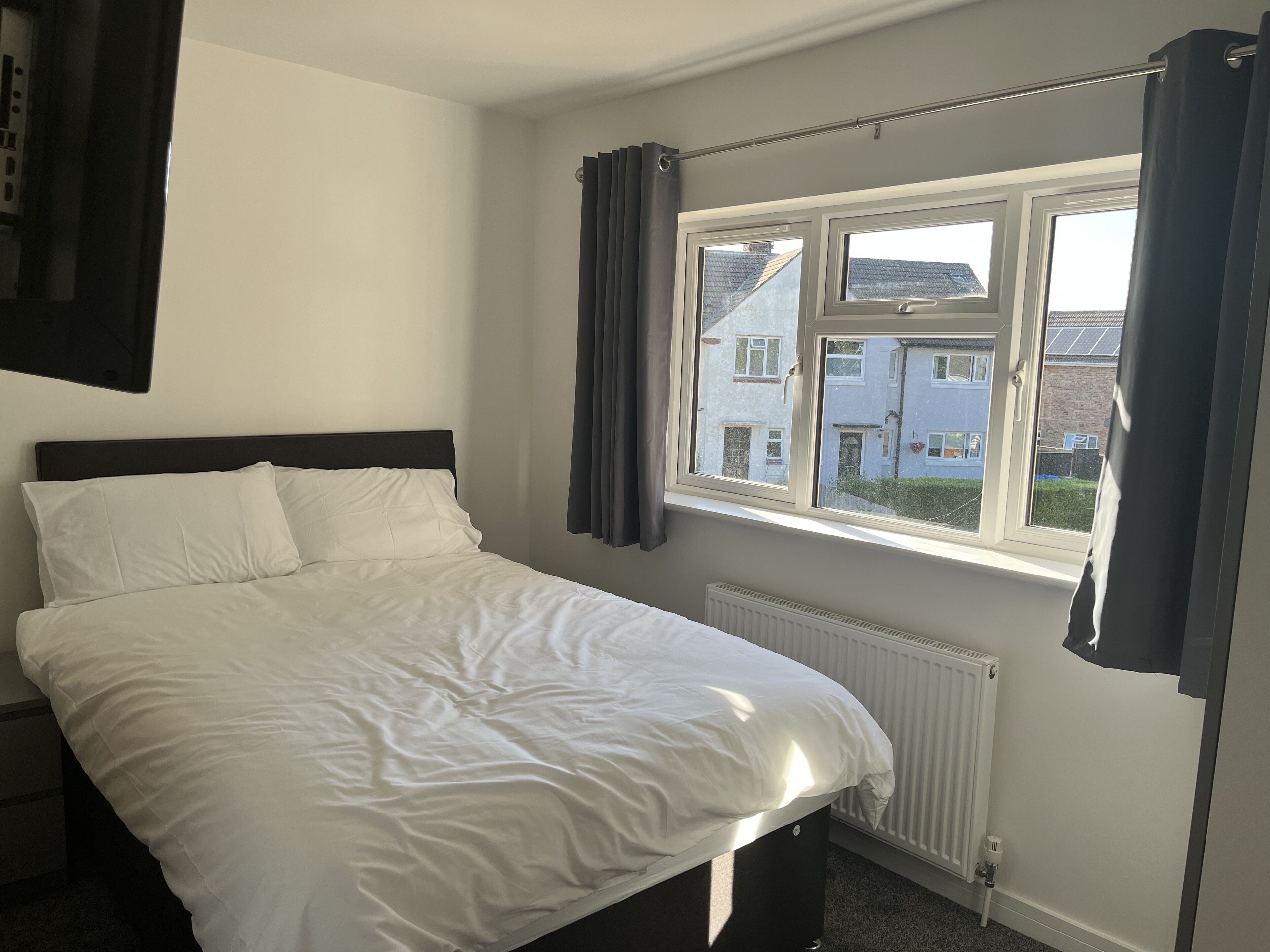 Une chambre à coucher avec un lit, une fenêtre avec des rideaux et une vue sur les bâtiments à l’extérieur.