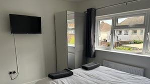 A bedroom with a bed, a TV mounted on the wall, a window with a view of the outside, and a radiator.