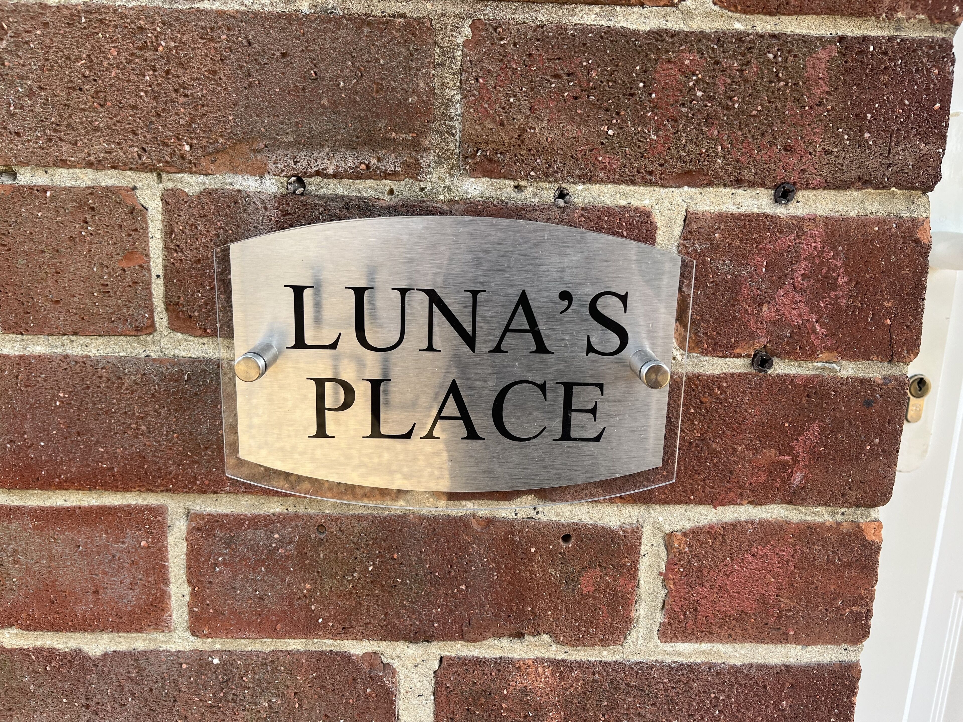 Een metalen bord met de tekst 'LUNA'S PLACE' bevestigd aan een bakstenen muur.