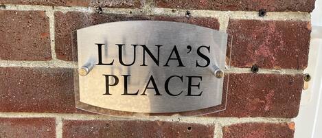 Een metalen bord met de tekst 'LUNA'S PLACE' bevestigd aan een bakstenen muur.