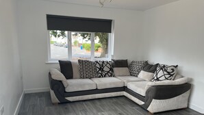 A modern living room with a sectional sofa, a large window, and a view of the street.
