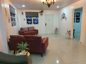 A spacious living room with a large sofa, a smaller armchair, and a coffee table with a plant. There is a door leading to another room and a small table with decorative items. - 2 Bed Apartment - Sleeps 4 - Parking - Wifi (Georgetown)
