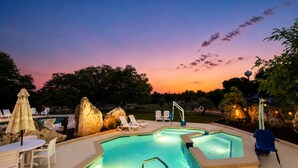 Una piscina con sillas de descanso y una mesa, rodeada de rocas y árboles.