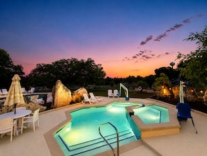 Ein Pool mit Liegestühlen und einem Tisch, umgeben von Steinen und Bäumen.