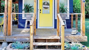 Una casa azul con puerta amarilla, porche de madera y plantas en macetas.