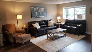 Ein Wohnzimmer mit zwei schwarzen Ledersofas, einem Holztisch, einem braunen Sessel und einer Weltkarte an der Wand.