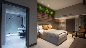 Ein modernes Schlafzimmer mit Bett, Nachttisch, Stuhl und einem Badezimmer mit Dusche und Waschbecken.