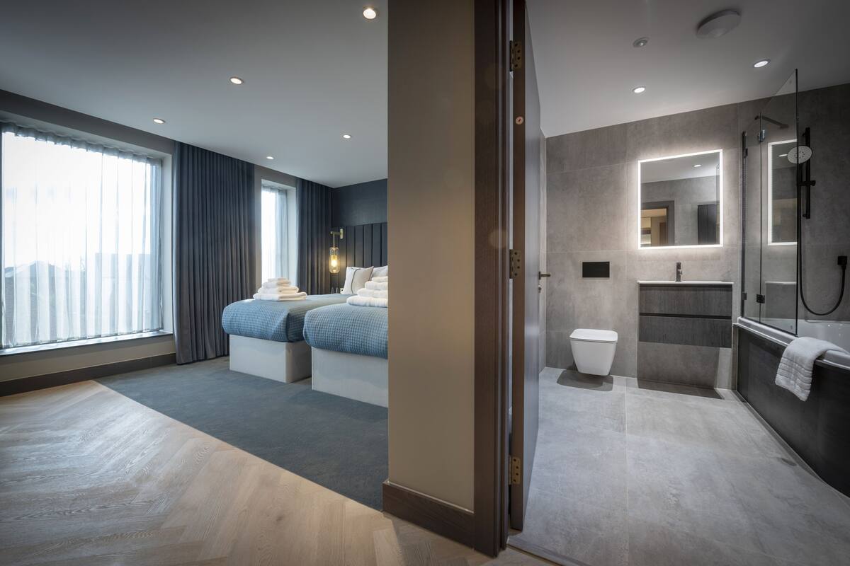A modern hotel room with a large bed, a separate bathroom, and a view of the city.
