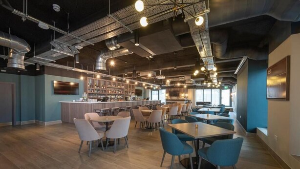 Ein modernes Restaurant mit Barbereich, verschiedenen Sitzmöglichkeiten und freiliegenden Lüftungsrohren an der Decke.