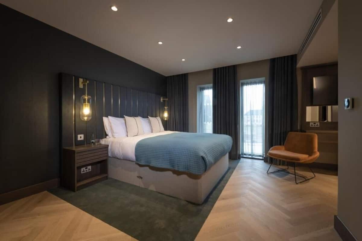 A modern bedroom with a large bed, bedside tables, a chair, and a wall-mounted TV.