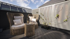 Eine Dachterrasse mit Korbmöbeln, einem kleinen Tisch und Kübelpflanzen.