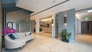 Eine moderne Lobby mit einer gebogenen weißen Couch, einer Zimmerpflanze und einem Empfangstisch im Hintergrund.