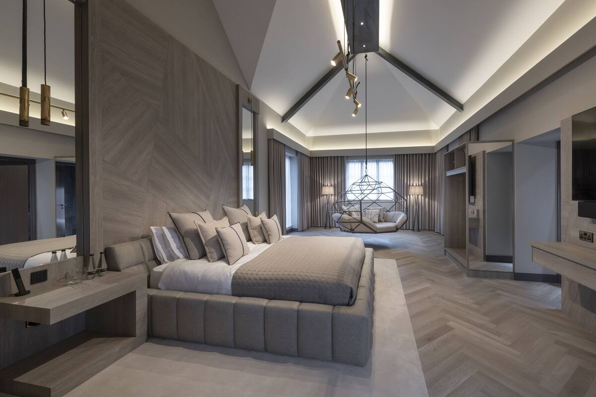 A modern bedroom with a large bed, bedside tables, a seating area, and a chandelier.