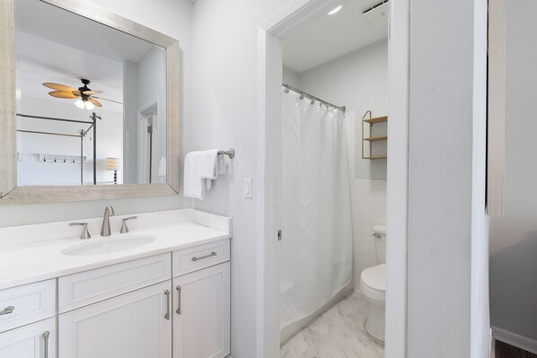A modern bathroom with a white vanity, a ceiling fan, a shower curtain, and a toilet.