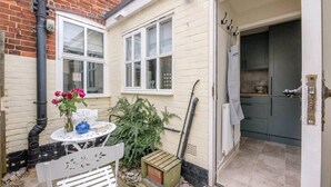 A small, cozy kitchen with a white door, a small table with a vase of flowers, and a bench outside.
