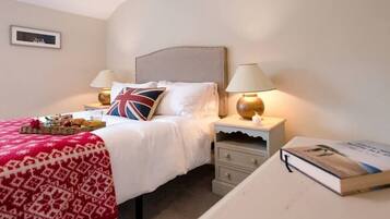 A neatly made bed with a red and white patterned blanket, a pillow with a Union Jack design, two bedside lamps, a bedside table with a book, and a framed picture on the wall.