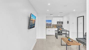 A modern living room with a wooden coffee table, a grey sofa, and a view to a kitchen with white cabinets and a dining area.