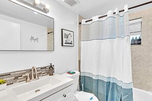 Un baño con lavamanos blanco, un espejo, inodoro y cortina de ducha.