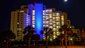 Hotel com várias andares, varandas iluminadas e uma torre central em azul vibrante.