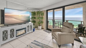 Una sala moderna con un televisor de pantalla plana grande, un sofá color beige y un balcón con vista al océano.