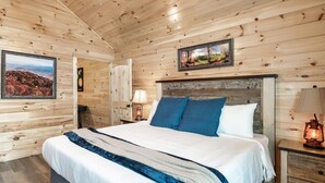 A wooden-paneled bedroom with a large bed, a nightstand with a lamp, and a framed picture on the wall. - 1 Min to Parkway|4 King BRs|Hot Tub|Pool|Dogs (Pigeon Forge)