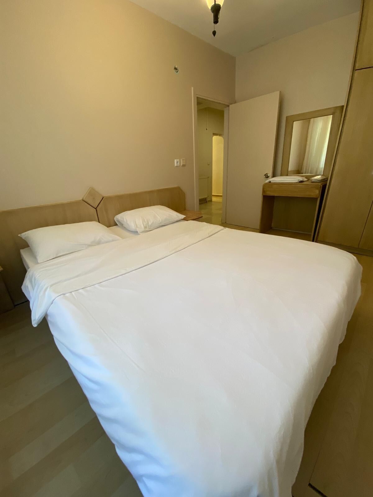 Una cama bien tendida en una habitación de hotel, con cabecera de madera, una mesita de noche y un espejo encima.