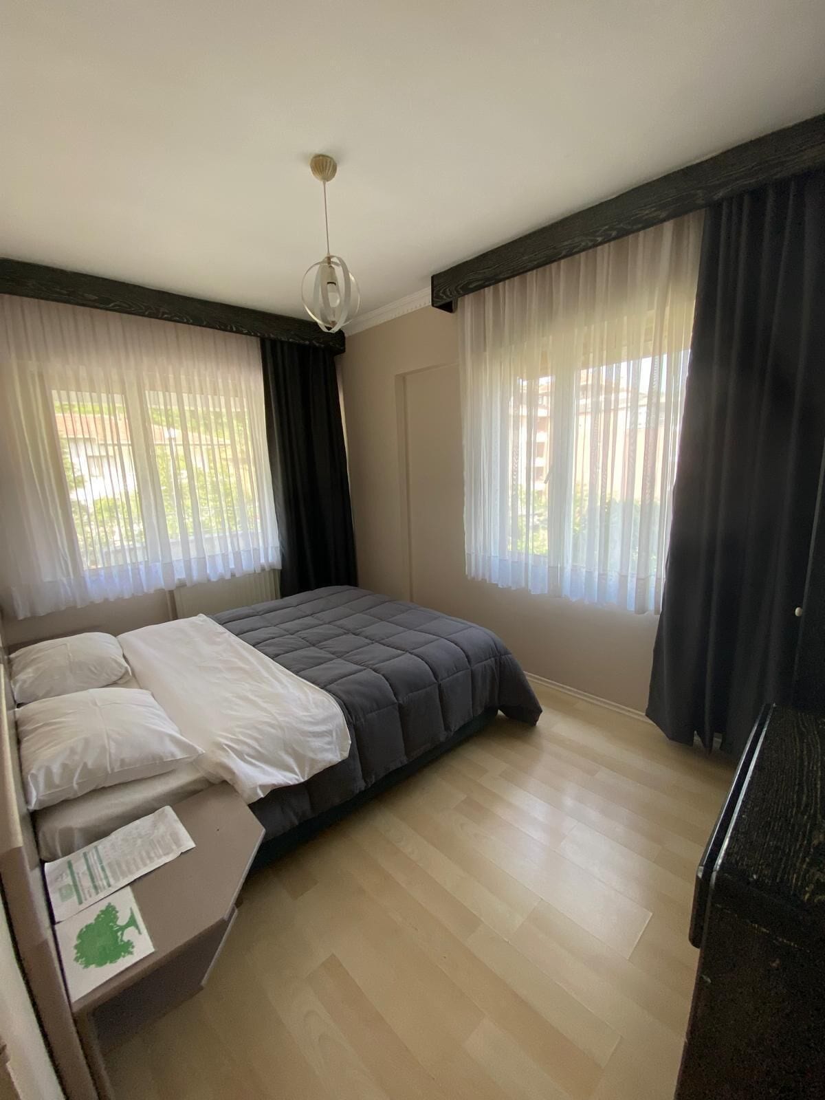 A bedroom with a bed, a desk, and two windows with curtains.