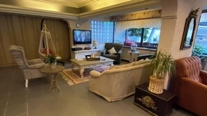 Amplia sala de estar con un sofá grande, una mesa de centro y un televisor. Hay un sillón colgante y una pequeña mesa con una planta.
