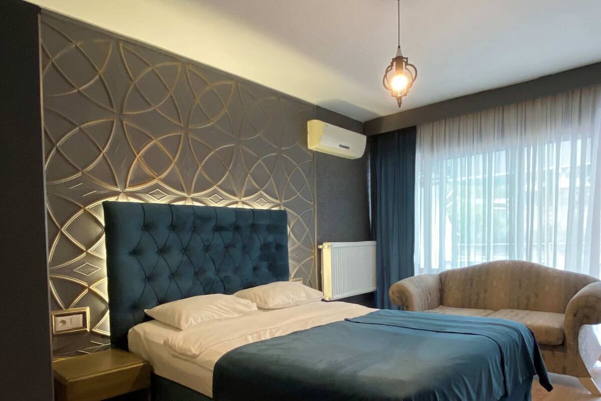 Ein modernes Schlafzimmer mit einem großen Bett, einem Nachttisch, einer Couch und einem dekorativen Wandmuster.